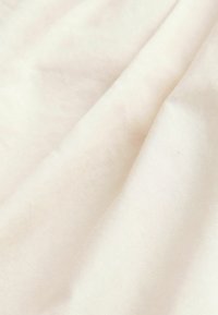 Gros plan d'un tissu doux blanc cassé avec des plis légers et une texture lisse sous la lumière naturelle.