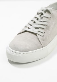 Baskets en daim gris clair avec semelle en caoutchouc blanche et lacets gris assortis, vues en angle de face sur fond blanc.