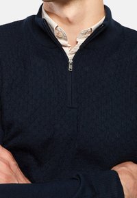 Maglione zip con cappuccio in tessuto navy con motivo a maglia testurizzata e tessuto interno a contrasto. Presenta una chiusura con zip argentata.