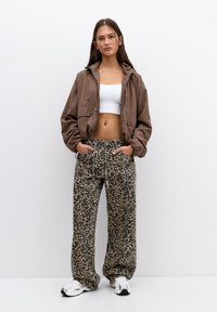 Hnedý skrátený kabát, biely crop top a voľné nohavice s leopardím vzorom. Textúrovaná látka s regulovateľným pásom a bočnými vreckami. Biely tenisky.