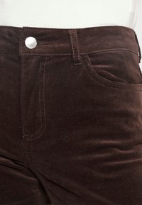 Bruna kordfläskbyxor med en strukturerad yta, som har en silverfärgad knapp, sidofickor och kontrasterande sömmar på midjan.
