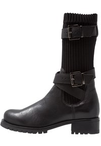Bota de cuero negro hasta el tobillo con caña de punto acanalado, destacando pliegues horizontales, una banda ancha con detalles de hebilla y una suela de goma plana.