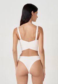 Costume da bagno bianco a due pezzi con reggiseno incrociato sul retro e spalline regolabili, e slip a vita alta, realizzato in materiale liscio ed elastico.