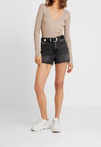 Beige geribbelde langemouwen top met een V-hals, gecombineerd met hooggewaiste zwarte denim shorts met franje aan de zijkanten, vastgemaakt met een zilveren gespriem.