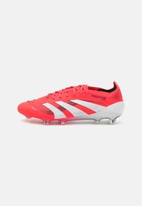 Red and white soccer cleats with a textured synthetic upper, featuring a low-cut design, lace closure, and transparent studs for traction.