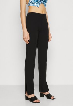 Black straight-leg trousers with side slits, made from lightweight fabric. Paired with black open-toe block-heeled shoes.
