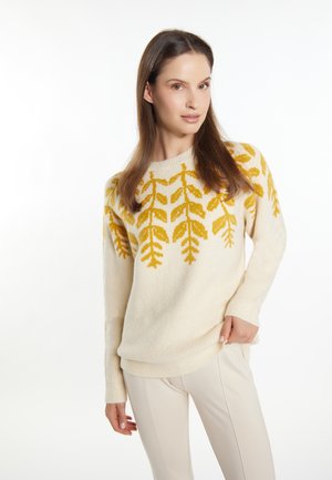 Pull crème avec un motif de feuille jaune sur la poitrine, à manches longues et à coupe décontractée, associé à un pantalon beige clair.