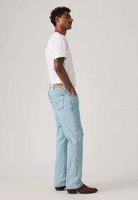 Φωτεινό γαλάζιο τζιν με ίσια γραμμή, φορεμένο με λευκό t-shirt, σε συνδυασμό με καφέ δερμάτινες μπότες. Διαθέτει δερμάτινη ετικέτα στο πίσω μέρος.