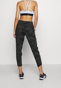 Grå kamouflerade joggers med elastisk midja och smalnande ben, i kombination med en ljusblå sport-bh med flera band.