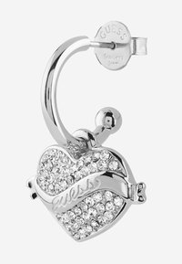Srebrny kolczyk w kształcie serca z kryształowymi ozdobami i zawieszką w kształcie pętli, z wygrawerowanym logo "Guess" na odwrocie.