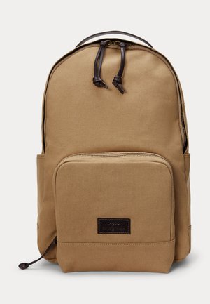 Béžový plátený batoh s predným vreckom na zips a tmavohnedými koženými ťahadlami na zips a nášivkou s logom.