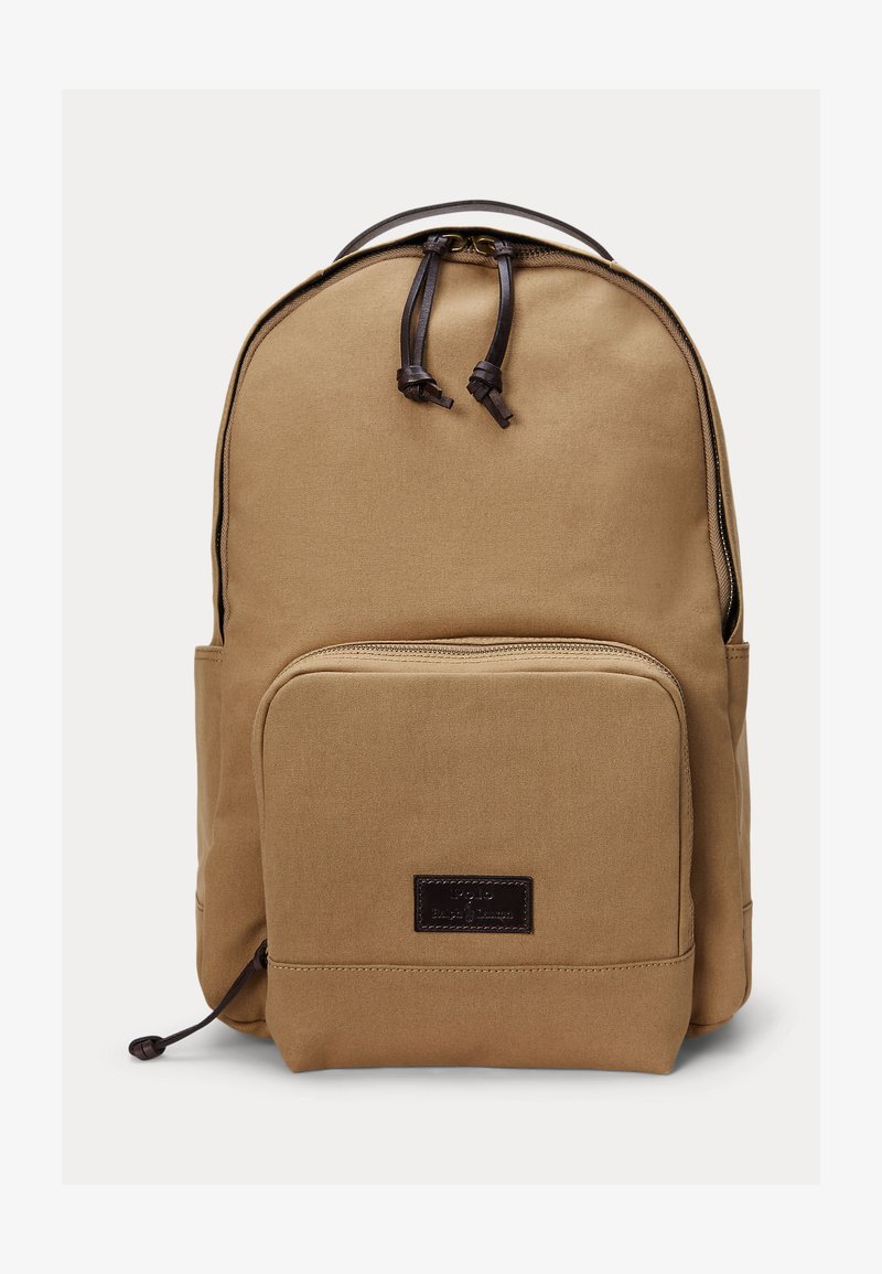 Béžový plátený batoh s predným vreckom na zips a tmavohnedými koženými ťahadlami na zips a nášivkou s logom.