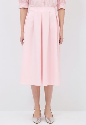 Jupe plissée rose clair, longueur genou, en tissu lisse. Dotée d'une taille ajustée et de poches latérales, associée à des chaussures métalliques.