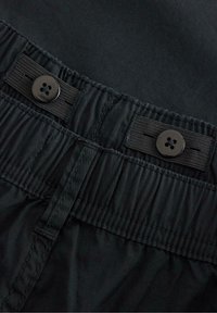 Pantaloni corti neri in tessuto con vita elasticizzata, due bottoni neri e dettagli di cucitura. La texture sembra liscia e resistente.