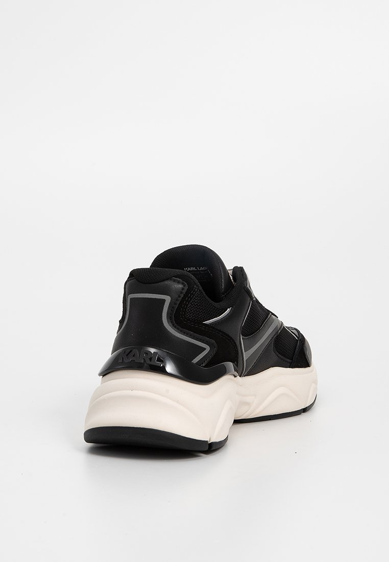 Chaussure de sport noire avec un dessus texturé, des accents gris contrastants et une semelle robuste. Présente un marquage à l'arrière et un design pour un ajustement sécurisé.