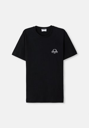 T-shirt en coton noir avec un col rond. Présente un petit design graphique blanc sur la poitrine. Manches courtes et ourlet droit.
