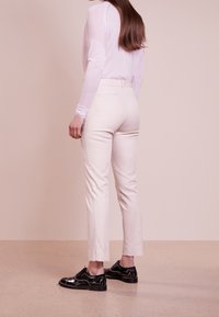 Kremowe dopasowane spodnie o gładkiej fakturze, z kieszeniami z tyłu, w połączeniu z czarnymi, ćwiekowanymi butami eleganckimi.