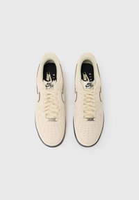 Nike Air Force 1 sneakers i cremefarve, med en perforeret tåboks, beige snørebånd, sorte accenter og tekstureret gummisul.