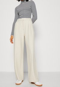 W paski golf w kolorze granatowym i białym, w połączeniu z beżowymi spodniami o wysokim stanie i szerokich nogawkach, cechującymi się gładką fakturą oraz plisowanym wzorem.