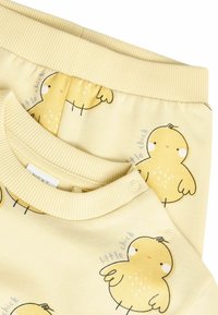 Dzeltena kokvilnas apģērba komplekts ar ribotu kakla izgriezumu un elastīgu jostu, ar vistas zīmējumiem un vienkāršām melnām kontūrām.