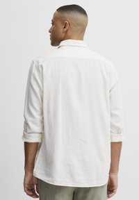 Camicia bianca in lino con una vestibilità comoda, maniche lunghe arrotolate. Presenta un colletto a punta e orlo arrotondato. Texture morbida con design minimalista.