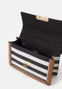 Stripet håndtaske med sort og hvid striber, tan-detaljer, guldhardware og en lynlåslomme indeni. Magnetlukning ved toppen.