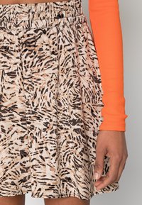 Gonna corta realizzata in tessuto leggero con una stampa animale astratta nei toni beige, nero e marrone; vita elasticizzata.