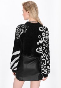 Schwarzer, flauschiger, verkürzter Pullover mit gemischten Tiermustern in Weiß, kombiniert mit einem Lederrock. Der Pullover hat voluminöse Ärmel und ein strukturiertes Design.