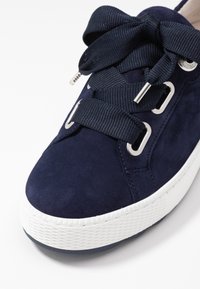 Sneaker in suede blu navy con suola in gomma bianca testurizzata, caratterizzata da lacci oversized blu navy, occhielli metallici e una punta arrotondata.