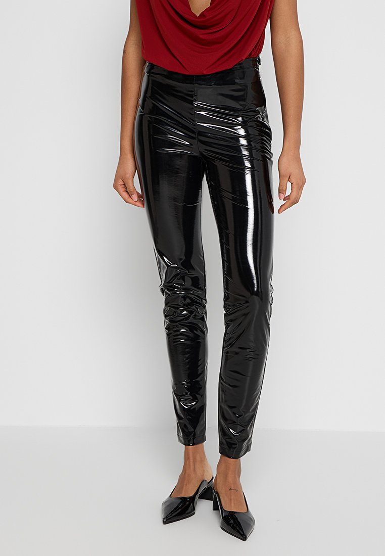 Schwarze, glänzende, enganliegende Hosen mit glatter Textur. Verfügt über eine glatte Oberfläche und schmale Beine, kombiniert mit spitzen schwarzen Absätzen.