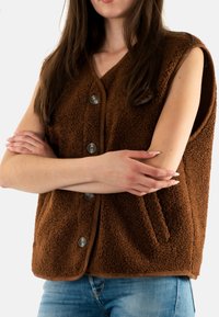 Gilet senza maniche in felpa marrone con scollatura a V, grandi bottoni e tasca laterale, caratterizzato da una superficie testurizzata e rifiniture a contrasto.