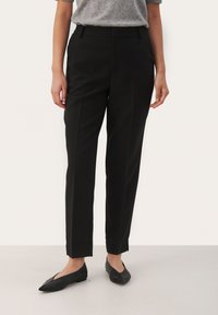 Black tailored trousers with a straight leg design, featuring a smooth fabric, crease detail, and side pockets. Styled with black flat shoes.