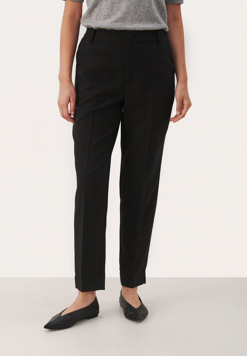 Black tailored trousers with a straight leg design, featuring a smooth fabric, crease detail, and side pockets. Styled with black flat shoes.