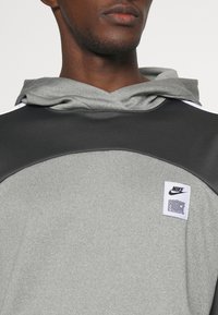 Felpa Nike caratterizzata da una palette di colori grigia e nera, tessuto testurizzato, un ampio cappuccio e un patch con il logo che reca la scritta "FORCE".