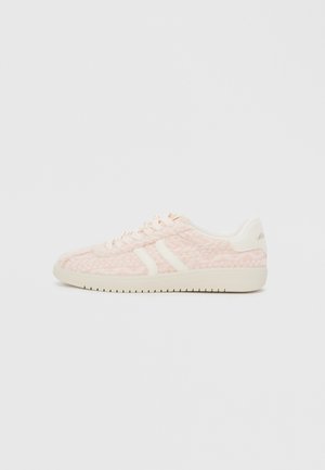 Sneakers rosa chiaro con un upper in tessuto testurizzato, caratterizzati da accenti e lacci bianchi, una suola piatta in gomma e un branding discreto sul tallone.