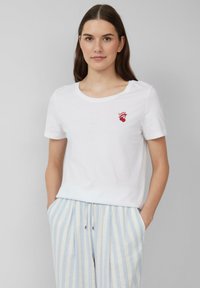 Witte katoenen T-shirt met korte mouwen en een ronde hals, met een kleine rode geborduurde graphic boven het linkerbovenstuk.