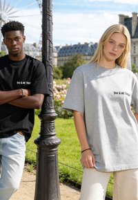 Deux jeunes adultes se tiennent près d'un lampadaire dans un parc, portant des t-shirts noirs et gris sur lesquels est écrit « YOU & ME TONIGHT ».