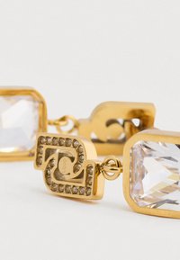 Χρυσές σκουλαρίκια που διαθέτουν ορθογώνιους διαυγείς κρυστάλλους, πολύπλοκες λεπτομέρειες με μικρές πέτρες και έναν στιλιζαρισμένο σχεδιασμό συνδέσμου.