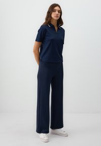 Navy blue polo shirt with a zip and short sleeves, paired with wide-leg navy trousers, both made of smooth, soft fabric. White sneakers.