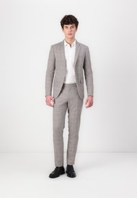 Graues Karo-Anzug mit taillierter Passform, strukturiertem Stoff, einreißigem Blazer und geraden Hosen, kombiniert mit einem weißen Hemd und schwarzen Schuhen.