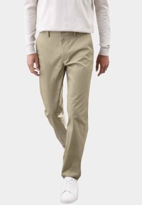 Pantalones beige de tela suave, con un diseño de pierna recta y cierre de botón. Combinados con zapatillas blancas, creando un look neutro.