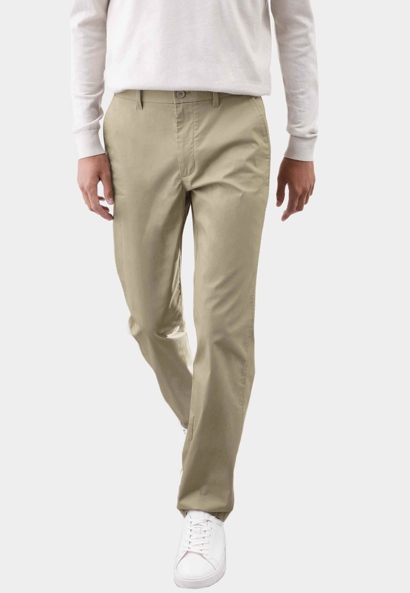 Pantalones beige de tela suave, con un diseño de pierna recta y cierre de botón. Combinados con zapatillas blancas, creando un look neutro.