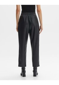 Czarne spodnie z imitacji skóry w luźnym kroju, z elastycznym pasem i jedną tylną kieszenią. Gładka tekstura i długi krój.