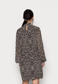 Blommönster, genomskinlig svart klänning med långa ärmar, hög krage och en detalj med nyckelhål i ryggen. Elastisk midja och flödande silhuett.