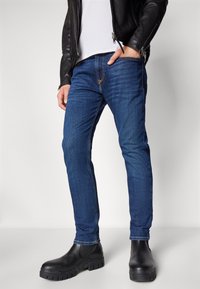 Jeans de mezclilla azul con un corte ajustado y un sutil desvanecimiento, combinados con botas negras hasta el tobillo y una chaqueta de cuero negra.