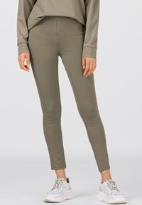 Olivgrön leggings i ett mjukt, stretchigt material med en åtsittande design. Kombineras med vita och grå sneakers som framhäver komfort.