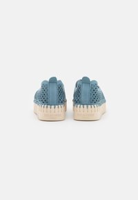 Zapatos azul de ante sin cordones con diseño perforado y suela de goma texturizada en color beige. Presentan un respaldo redondeado y el nombre de la marca embosado en la suela.