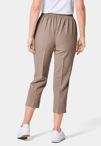Beige Caprihosen mit einem elastischen Bund, die eine glatte Textur und einen geraden Schnitt aufweisen, kombiniert mit weißen Turnschuhen.