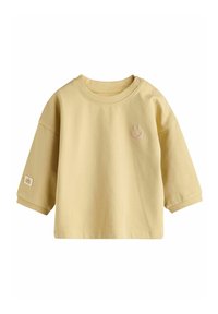 Hellgelbes Baumwoll-T-Shirt mit kurzen Ärmeln, rundem Halsausschnitt und einem kleinen pinken lachenden Gesichtdesign auf der Vorderseite. Mit seitlichem Druckknopfverschluss.