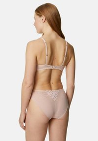 Set di lingerie rosa chiaro composto da un reggiseno trasparente con spalline regolabili e un perizoma abbinato con dettagli floreali sul retro.
